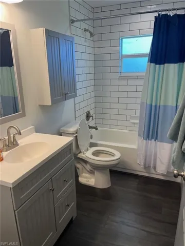 Full bathroom featuring wood-type flooring, vanity, toilet, and shower / tub combo with curtain