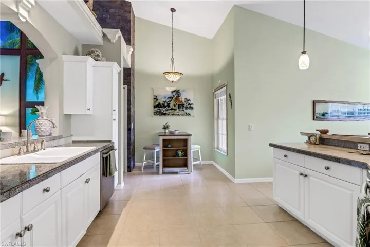 Kitchen featuring white cabinetry, decorative light fixtures, high vaulted ceiling, and stainless steel dishwasher