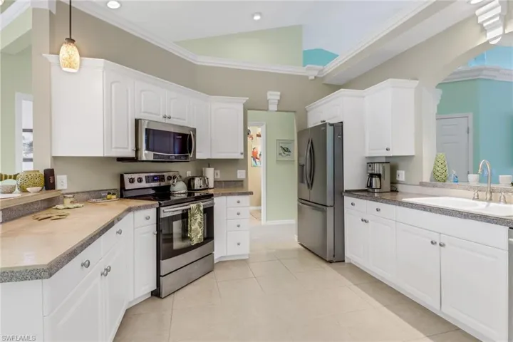 Kitchen featuring appliances with stainless steel finishes, crown molding, white cabinetry, decorative light fixtures, and light tile patterned floors