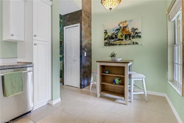 Kitchen with stainless steel dishwasher, white cabinets, and light tile patterned floors