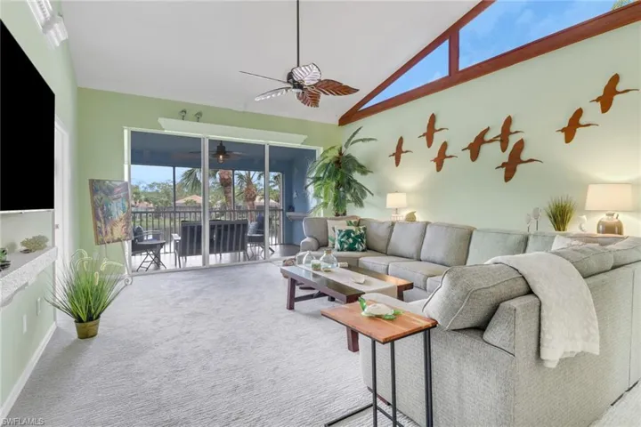 Carpeted living area with healthy amount of natural light, high vaulted ceiling, and ceiling fan