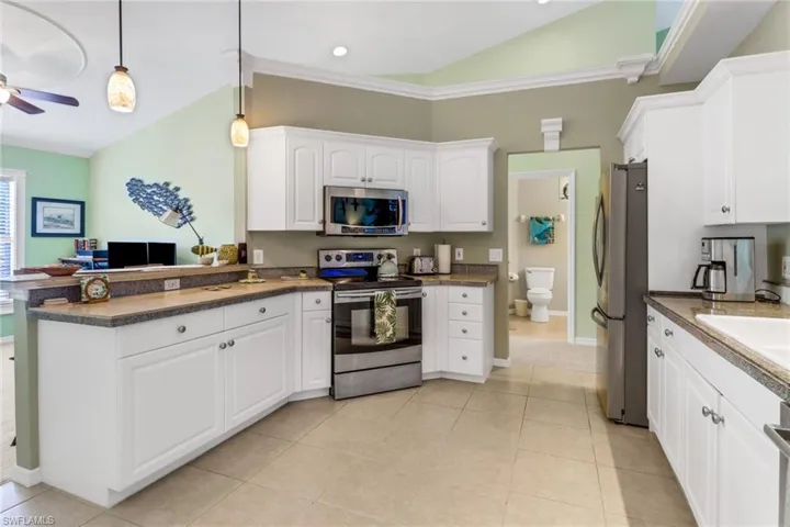 Kitchen with lofted ceiling, appliances with stainless steel finishes, white cabinets, dark countertops, and a peninsula