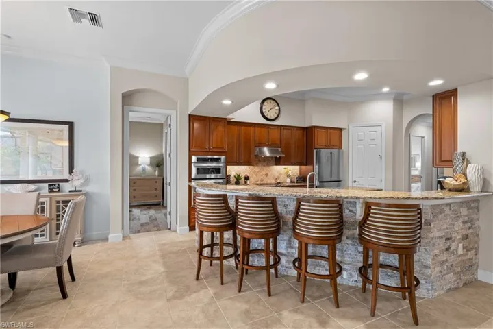 Kitchen featuring a breakfast bar area, arched walkways, a peninsula, light stone countertops, and wood finish cabinets
