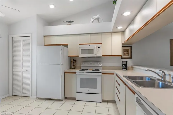 Kitchen with lofted ceiling, cream cabinets, white appliances, sink, and light tile floors