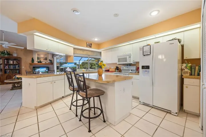 Kitchen with a kitchen breakfast bar, a peninsula, white appliances, white cabinets, and light tile patterned floors