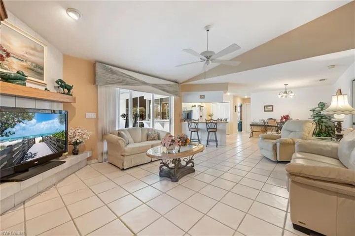Living area featuring vaulted ceiling, ceiling fan, light tile patterned flooring, a tile fireplace, and hanging lights