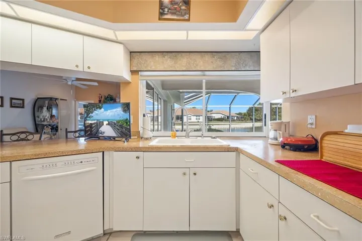 Kitchen with a sunroom, white cabinetry, white dishwasher, and light countertops