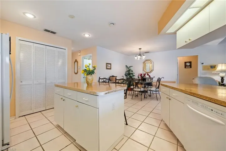 Kitchen with white dishwasher, freestanding refrigerator, white cabinets, a kitchen island, and light tile patterned flooring