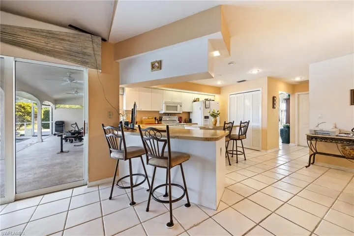 Kitchen with a peninsula, a kitchen bar, white appliances, white cabinetry, and a ceiling fan