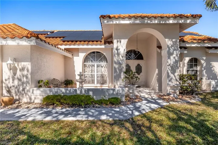 View of front with solar panels, stucco siding, a tile roof, and a front yard