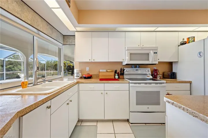 Kitchen featuring white appliances, light countertops, white cabinetry, and light tile patterned flooring