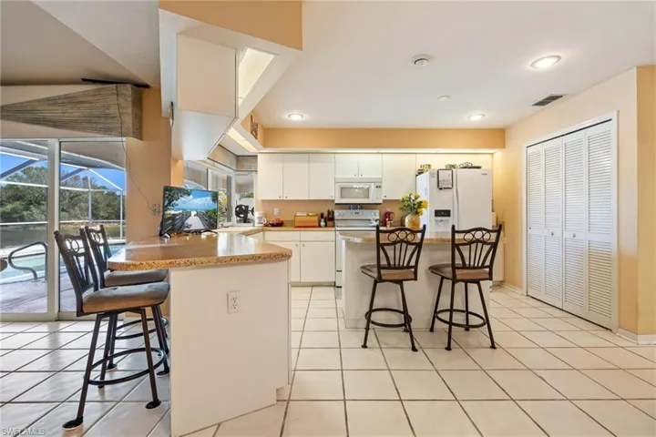 Kitchen featuring a kitchen bar, white appliances, a peninsula, and white cabinets