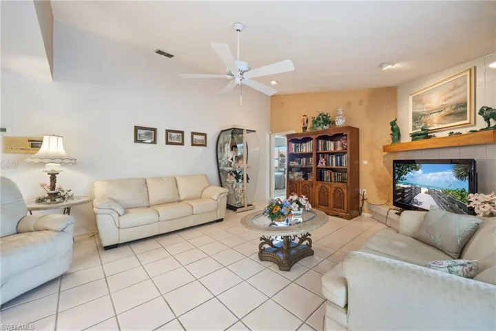 Living area featuring vaulted ceiling, ceiling fan, light tile patterned flooring, and a tiled fireplace