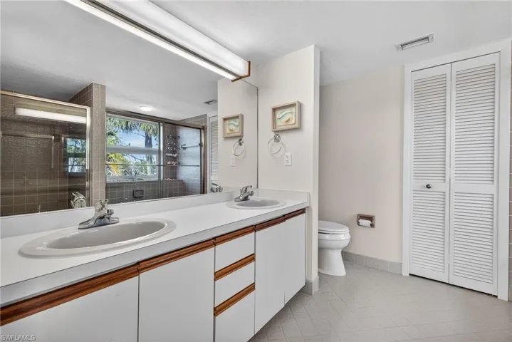 Full bathroom featuring double vanity, a stall shower, light tile patterned floors, and a closet