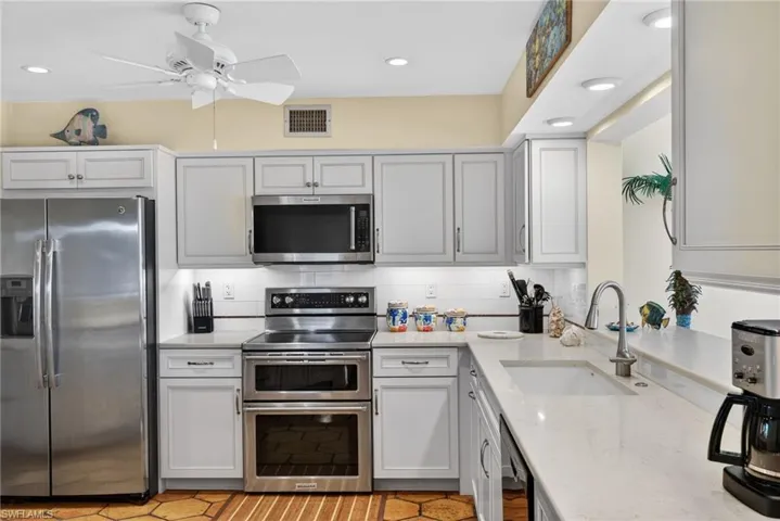 Kitchen with appliances with stainless steel finishes, light stone countertops, tasteful backsplash, recessed lighting, and a ceiling fan