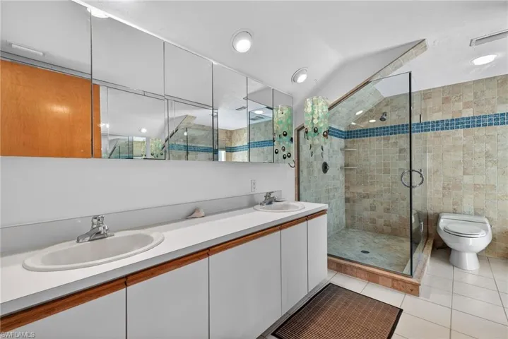 Primary Bathroom with double vanity, a shower stall, light tile patterned floors, and vaulted ceiling