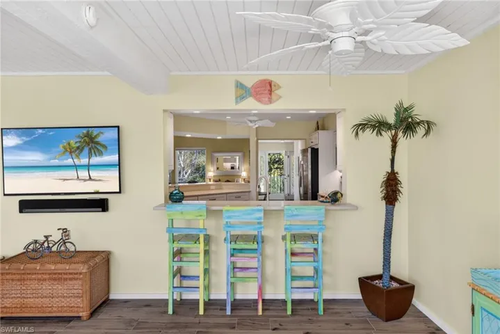 Family Room bar area featuring a wooden ceiling with exposed beams, freestanding refrigerator, ornamental molding, wood tiled floors, and light countertops