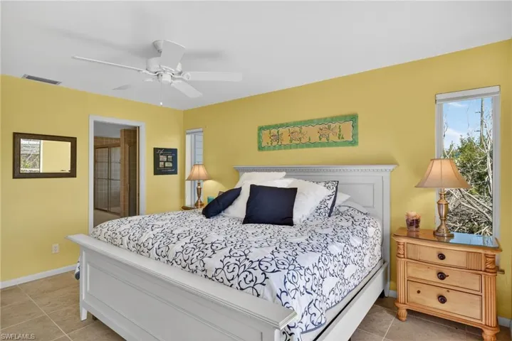 Bedroom featuring light tile patterned floors, connected bathroom, and a ceiling fan