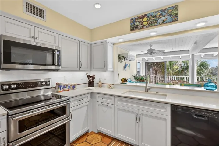 Kitchen featuring appliances with stainless steel finishes, decorative backsplash, ceiling fan, a wall mounted air conditioner, and white cabinets