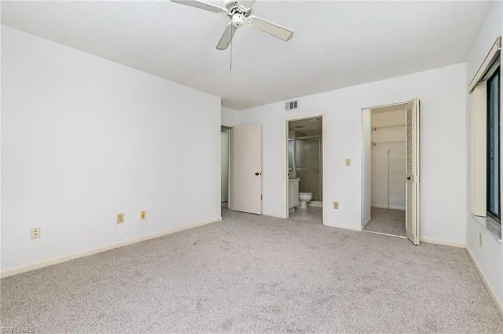 Unfurnished bedroom featuring carpet flooring, a textured ceiling, ensuite bathroom, and a ceiling fan