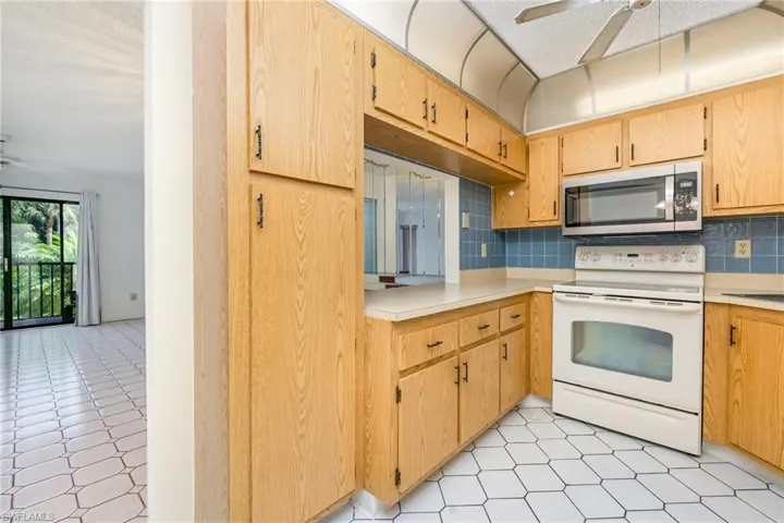 Kitchen with a ceiling fan, white electric range, backsplash, stainless steel microwave, and lofted ceiling