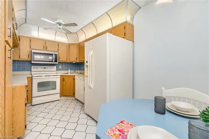 Kitchen featuring white appliances, ceiling fan, light countertops, tasteful backsplash, and a textured ceiling