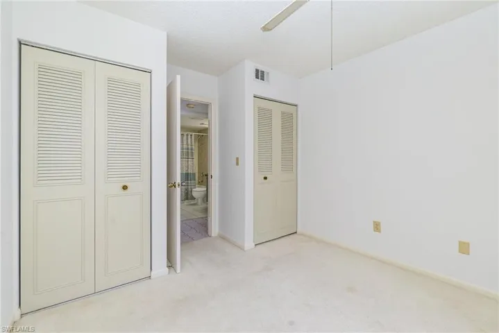 Guest bedroom with light colored carpet, two closets, a textured ceiling, and ceiling fan.