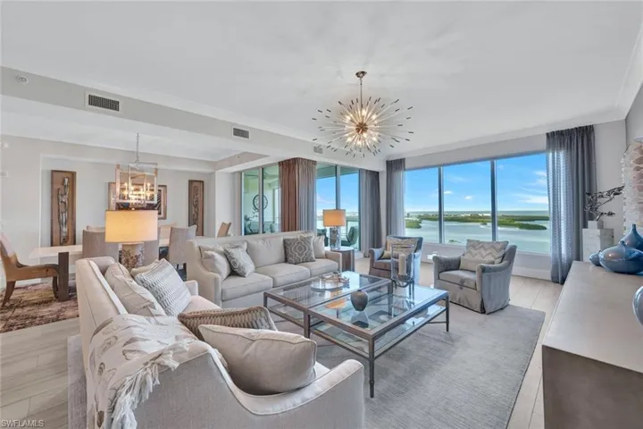 Living room features a gorgeous chandelier, wood look tile flooring and a spectacular water view.