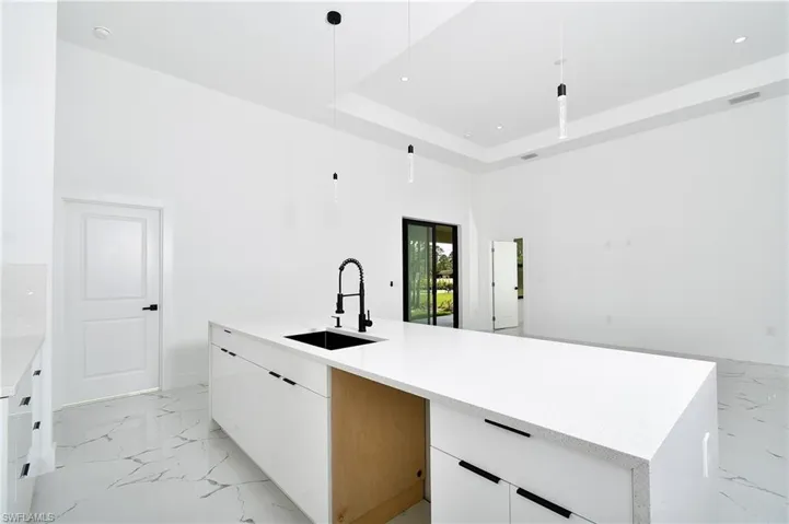 Kitchen with sink, white cabinetry, decorative light fixtures, a large island, and a raised ceiling