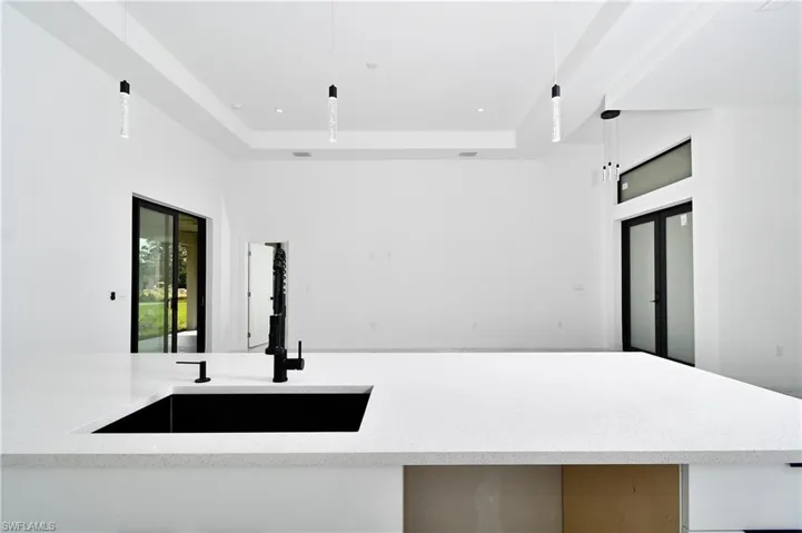 Kitchen with a tray ceiling, sink, light stone countertops, and decorative light fixtures