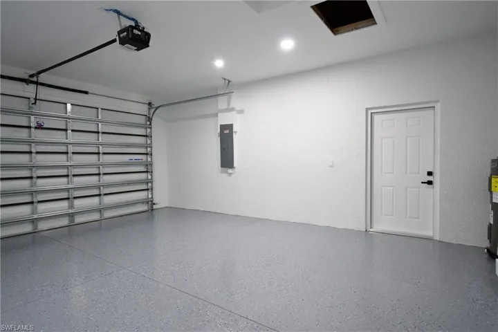 Garage with a garage door opener, electric panel, and electric water heater