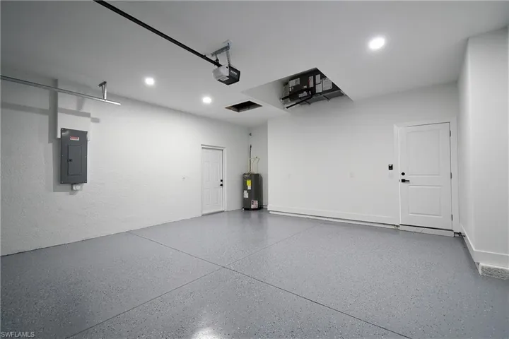 Garage with water heater, electric panel, and a garage door opener
