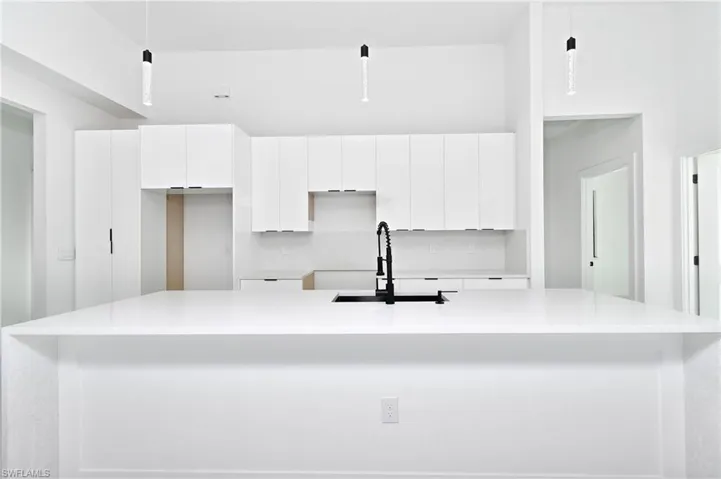 Kitchen featuring hanging light fixtures, white cabinetry, sink, and backsplash