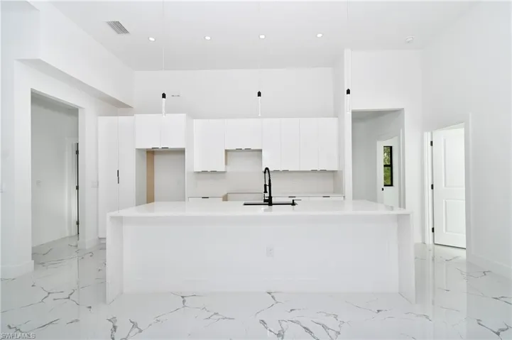 Kitchen featuring sink, pendant lighting, a towering ceiling, white cabinets, and a kitchen island with sink