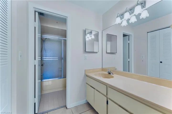 Bathroom with a closet, vanity, tile patterned flooring, and shower / bath combination with glass door