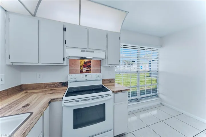 Kitchen with white range with electric stovetop, under cabinet range hood, and light tile patterned floors