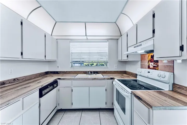 Kitchen with white appliances, under cabinet range hood, and light tile patterned flooring
