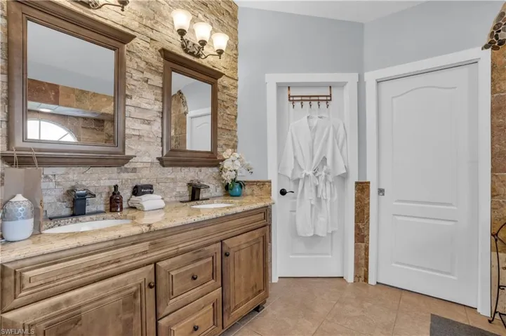 Full bath featuring double vanity, light tile patterned flooring, and decorative backsplash