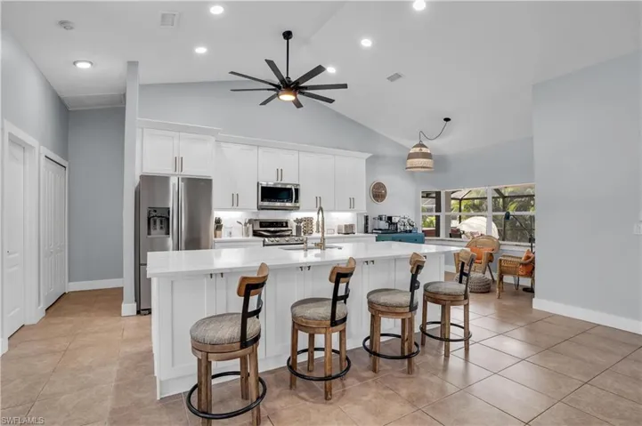 Kitchen featuring white cabinets, a breakfast bar, appliances with stainless steel finishes, an island with sink, and light stone countertops
