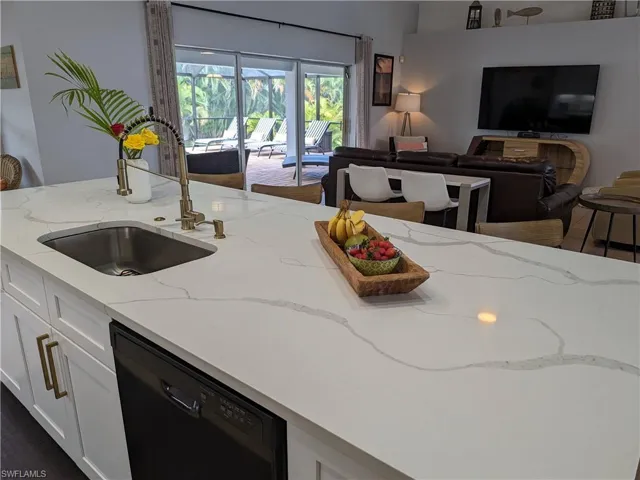 Kitchen with white cabinets, light stone countertops, black dishwasher, and open floor plan