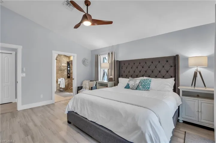 Bedroom with lofted ceiling, light wood-style flooring, ceiling fan, and connected bathroom