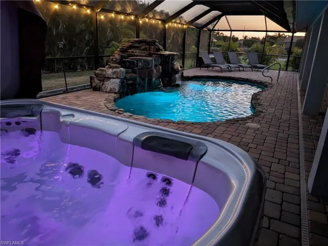 Pool at dusk with a sunroom, a lanai, an outdoor pool, a patio area, and an outdoor hot tub