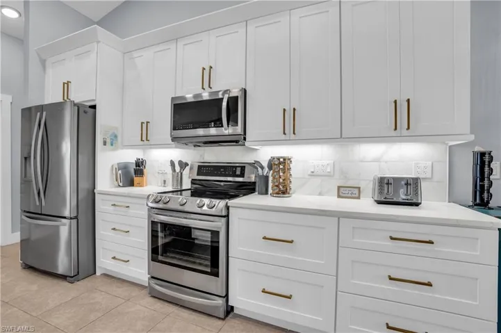 Kitchen featuring stainless steel appliances, tasteful backsplash, white cabinets, light tile patterned floors, and light stone countertops