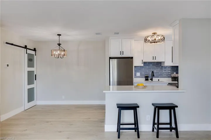 Kitchen with suspended lighting, a barn door, freestanding refrigerator, white cabinetry, and a peninsula