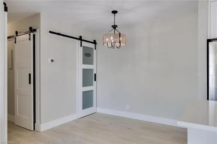 Unfurnished dining area featuring a barn door, light wood-style flooring, and a chandelier