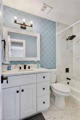 Full bath with vanity, wallpapered walls, and shower / tub combination