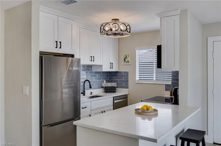 Kitchen with a breakfast bar area, stainless steel appliances, white cabinets, a peninsula, and backsplash
