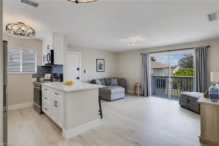 Kitchen featuring open floor plan, stainless steel appliances, white cabinets, light stone counters, and decorative backsplash