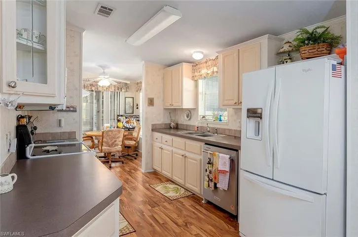 Kitchen featuring ceiling fan, light wood-type flooring, stainless steel dishwasher, white refrigerator with ice dispenser, and sink