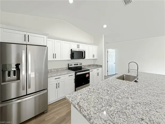 Kitchen with stainless steel appliances, light stone counters, white cabinets, lofted ceiling, and light wood finished floors